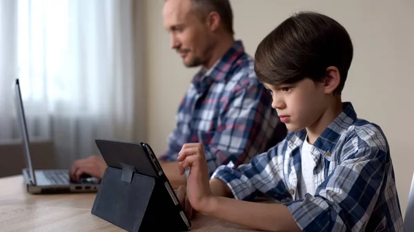 Male Kid Playing Game Tablet While Father Working Laptop Home — Stock Photo, Image