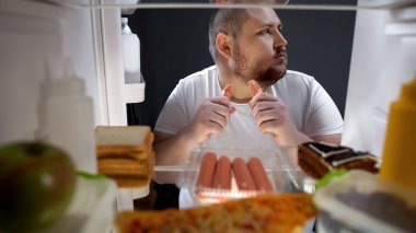 Bağımlısı adam gizlice gece buzdolabı, sağlıksız beslenme yakınındaki sosis yeme