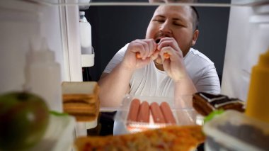 Bağımlısı genç adam yeme sosis buzdolabı, sağlıksız beslenme yakınındaki geceleri