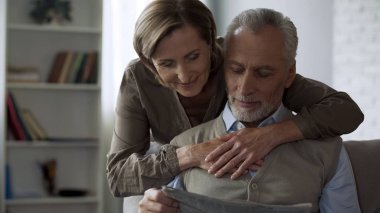 Kadın kocası sarılma yaşlanma, Erkek kanepede oturan ve gazete okuma seviyorum