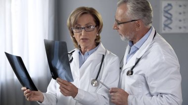 Experienced doctors discussing methods of treatment, comparing x-rays of joints clipart