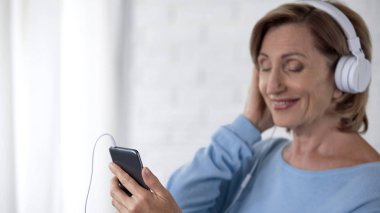 Emekli Bayan cep telefonu müzik dinlemek ve gülümseyen kulaklık