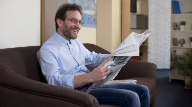Mutlu orta kırklı erkek okuma gazete, kanepeye, basın oturan rahat kişi