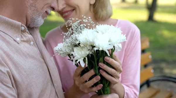 Šťastný Pár Zralých Přitulená Držení Kytice Bílých Květů Sedí Lavičce — Stock fotografie