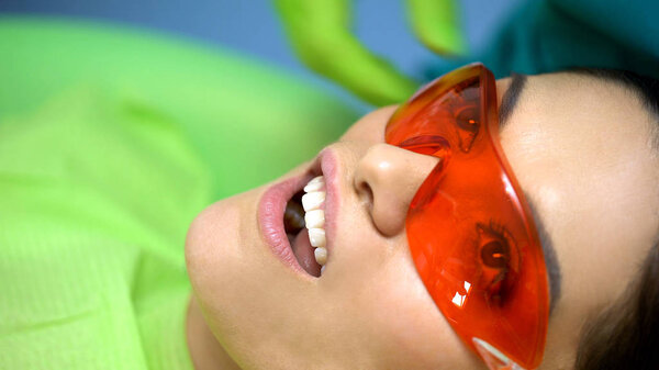 Женщина в защитных очках, излечивающая свет для современного лечения зубов
