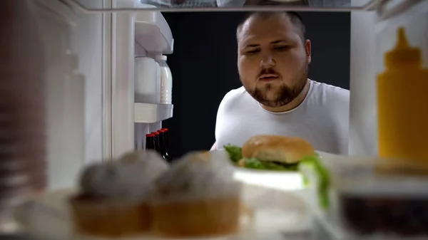 太りすぎの大きなハンバーガーは カロリーを取る若い男 夜に冷蔵庫を開く — ストック写真