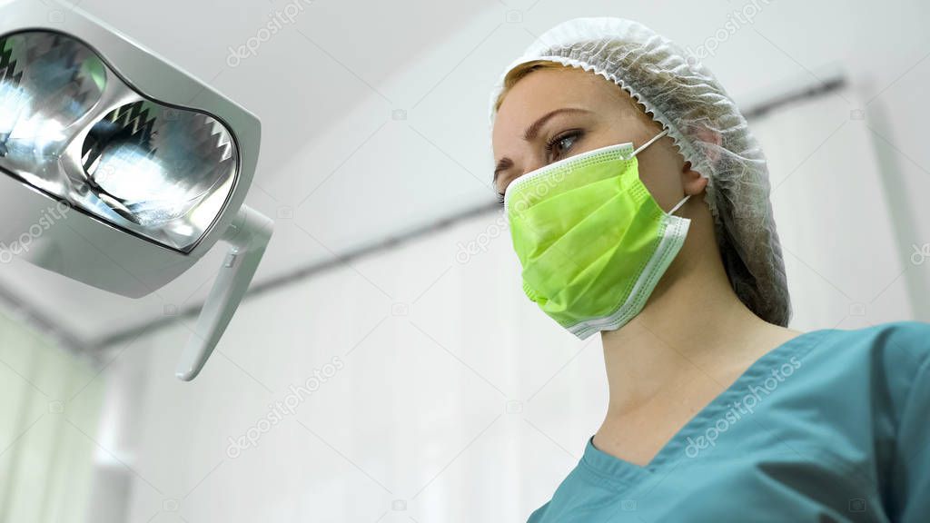 Female dentist wearing mask and cap before operation, professional services