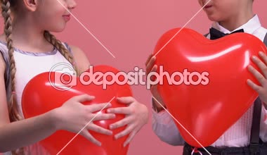 Kalp şeklinde balonlar tutarak ve kamera için aşk gülümseyen küçük çift