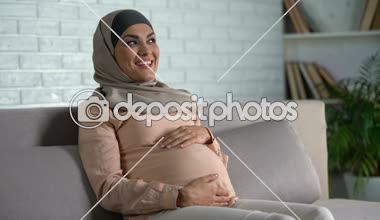 Müslüman kadın okşayarak göbek çocuk uyum taşıyan kanepede oturmuş bekliyor