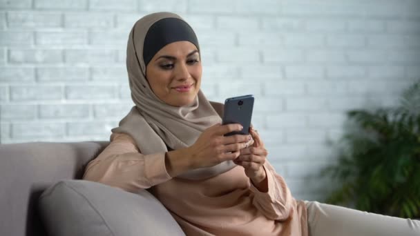 现代穆斯林女性打字消息上的智能手机 坐在家里的沙发 小玩意 — 图库视频影像
