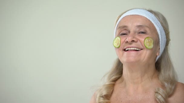 滑稽的快乐奶奶与黄瓜面膜在脸上咬一片 面带微笑 — 图库视频影像