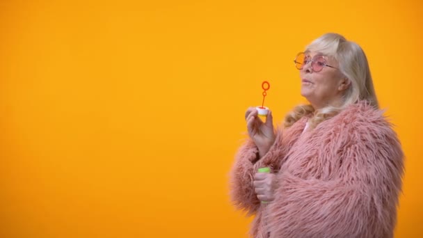 正面的老年妇女在滑稽的粉红色外套和圆形太阳镜做肥皂泡 — 图库视频影像