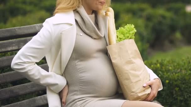 ショッピング バッグのベンチ 背部の痛みの残りの部分を持っていることで若い妊婦 — ストック動画