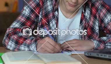 Yakışıklı öğrenci kameraya, gülümseyen masada, evde eğitim egzersiz yaparak