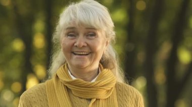 Gülümseyen yaşlı kadın kamera için poz el, güvenli yaşlılık ile mutlu sallayarak