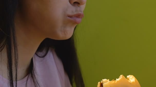 十几岁的女孩咬和慢慢咀嚼美味的汉堡 高热量的快餐 — 图库视频影像