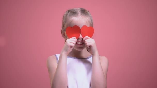 有趣的小女孩闭上眼睛与红色纸心脏隔离在粉红色的背景 — 图库视频影像