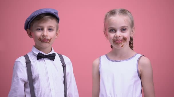 Alegre niño y niña sonriendo y comiendo caramelos de chocolate, celebrando la fiesta — Vídeos de Stock