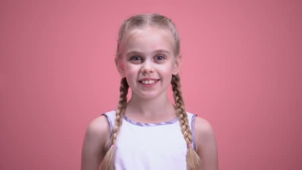 Маленька усміхнена дівчинка з косами, показуючи іграшкове серце на камеру крупним планом, благодійність — стокове відео
