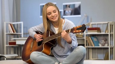 Young lady playing guitar in her room, writing song, dreaming of music career clipart
