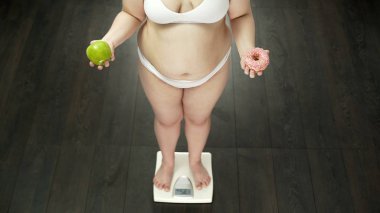 Kilolu kız ölçeklerde elma ve çörek, ayakta yemek seçim Diyet