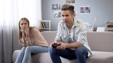 Unhappy girl looking at her boyfriend who indifferently playing video games clipart