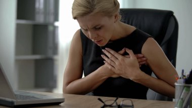Female manager working on computer, suffering from sharp chest pain, arrhythmia clipart