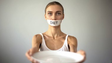 Slim girl with taped mouth showing empty plate, severe diet and self-destruction clipart