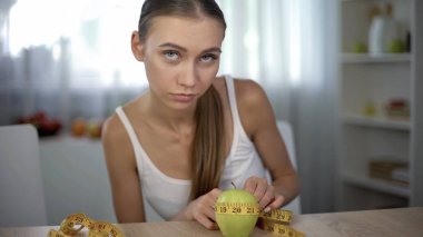 Anorexic girl measuring apple with tape, counting calories and body mass index clipart