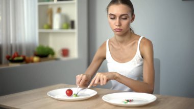 Girl eats spinach, looks at anti-obesity pills, drugs as easy way to lose weight clipart