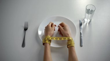 Hands tied with tapeline on empty plate, girl obsessed with counting calories clipart