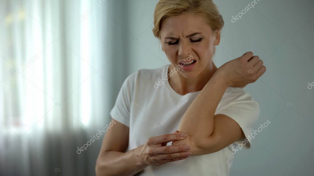 Blond woman suffering from elbow pain, holding her aching arm, injury and cramp