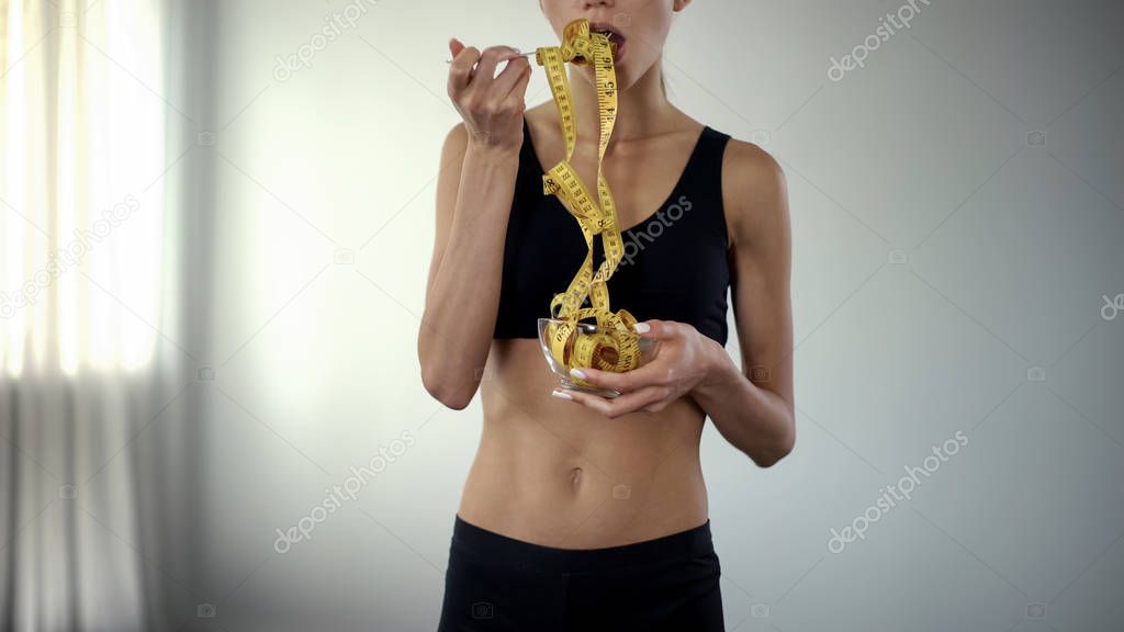 Fitness girl eating measuring tape, concept of bmi control, food restrictions