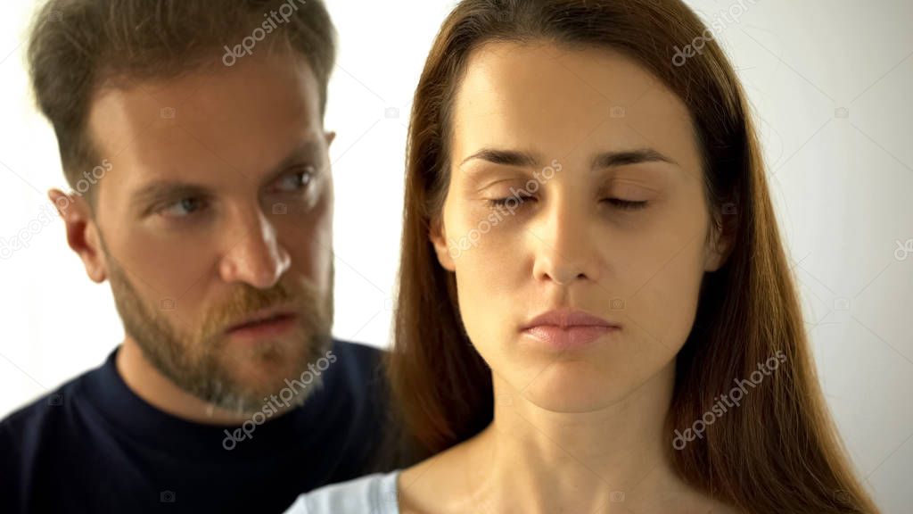 Man standing behind wife, sad lady with closed eyes hearing husband decisions