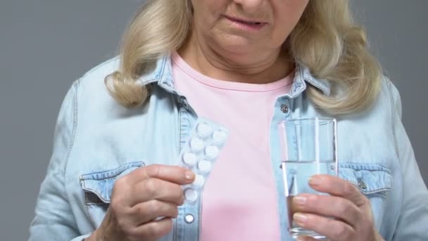 錠剤と水のガラスを保持している不幸な古い女性悲しげにため息は治療の疲れ — ストック動画