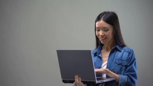 Laptop Ayakta Gri Arka Plan Üzerine Yazarak Neşeli Asyalı Kadın — Stok video