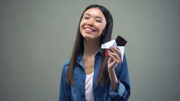 Atraente Menina Asiática Sorrindo Câmera Comendo Chocolate Escuro Propaganda — Vídeo de Stock