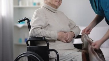 Tekerlekli sandalyeye mahkum battaniye ile hemşire kapsayan eski kadın hasta bakımı