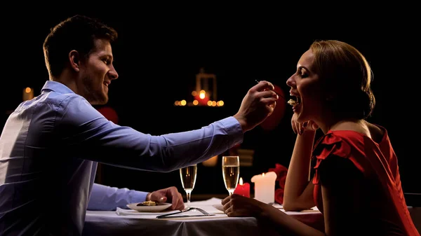 Handsome man feeding pretty lady, couple having romantic dinner at restaurant