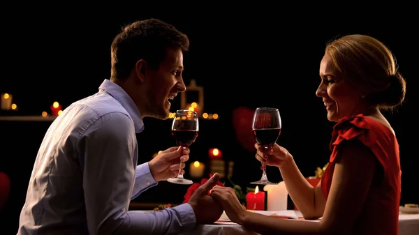 Sweet couple laughing, holding glasses with red wine, date in restaurant