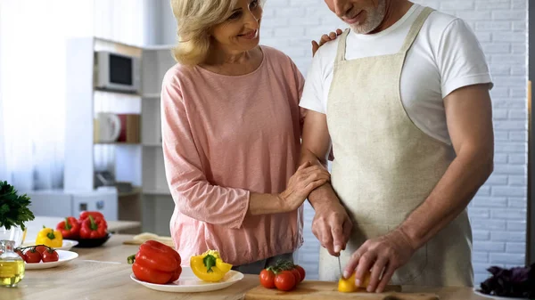 年长的丈夫在厨房里切新鲜的胡椒 妻子拥抱爱 — 图库照片