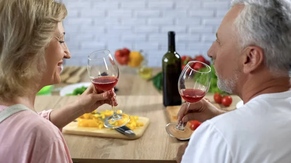 爱的老年夫妇拿着眼镜与红酒坐在家里的厨房 — 图库照片