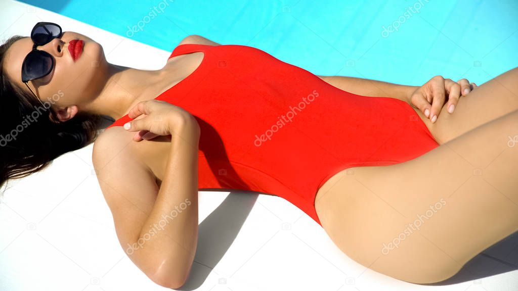 Seductive woman in swimwear relaxing near swimming pool at luxury resort