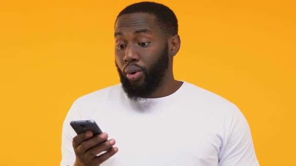 Удивленный Черный Мужчина Смотрит Смартфон Обновление Мобильного Приложения Желтый Фон — стоковое видео