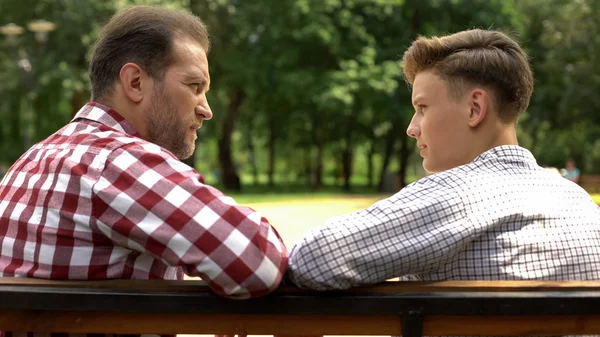 认真的儿子和爸爸在公园的长椅上聊天 父亲分享生活经验 — 图库照片
