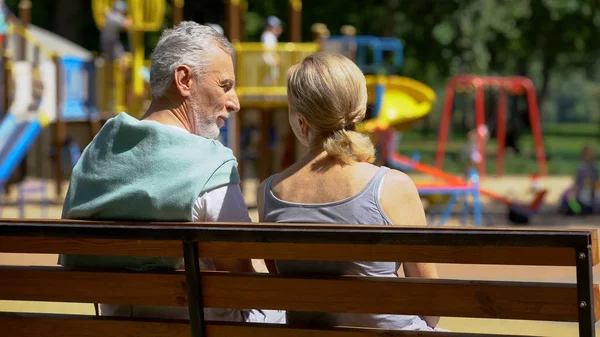Äldre Man Och Kvinna Som Kommunicerar Bänken Parken Titta Barnbarn — Stockfoto