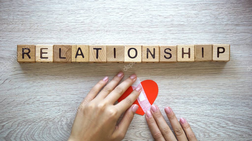 Relationship word on wooden cubes, female hands putting patch on paper heart