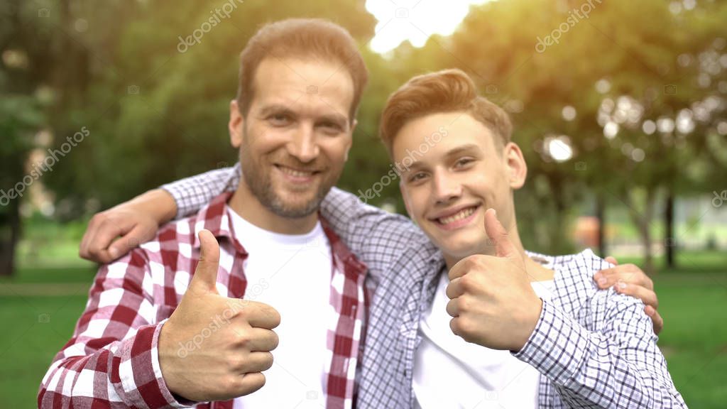 Happy son and father showing thumbs-up, enjoying pastime together, picnic