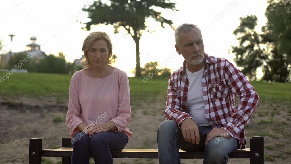 Elderly couple sitting on bench, sad man thinking about family problems, quarrel