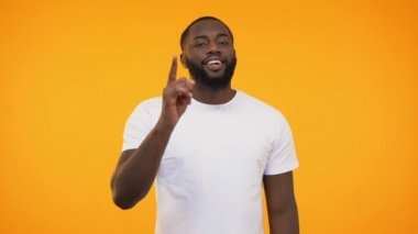 Afrikalı-Amerikalı adam kamera ve göz kırpıyor, işaret parmağı bilerek gülümseyen